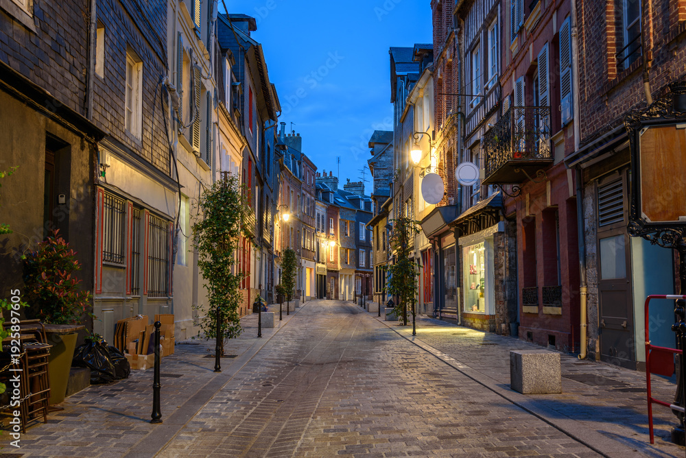 Fototapeta premium Deserted cobbled street lined with traditional residential buildings and shops at twilight in summer