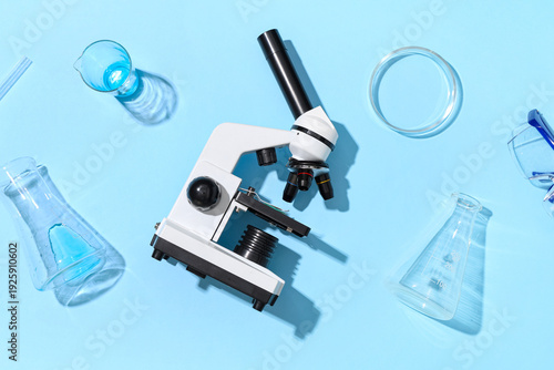 Modern microscope with safety glasses, petri dish and flasks on blue background