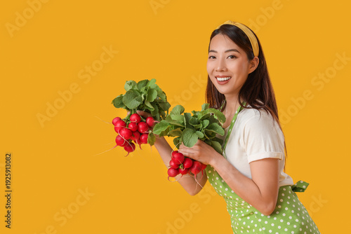Young Asian housewife with ripe radish on yellow background
