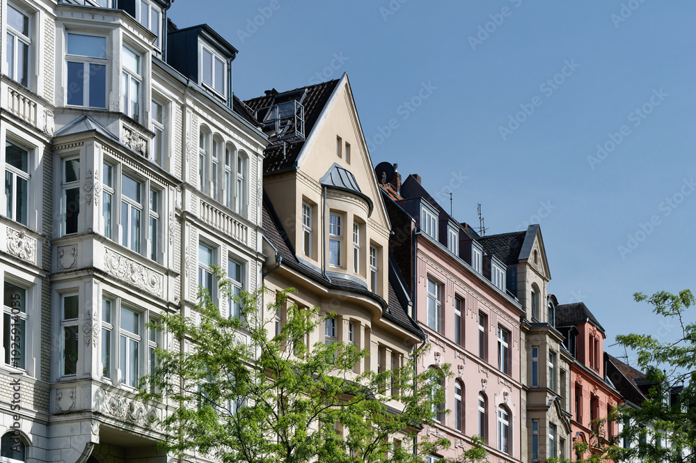 Fototapeta premium Row of colorful historicist style apartment buildings in Cologne Nippes. Featuring ornate bay windows and gables under a clear blue summer sky