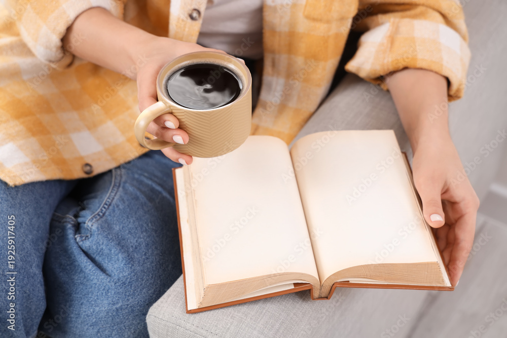 Obraz premium Young woman holding cup of hot coffee and book with blank pages on sofa at home, closeup