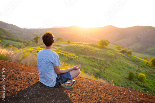 man practicing mindfulness on a rocky peak at sunset. Concept of mental health, inner peace and digital detox, with warm light, green landscape, freedom, tranquility and modern self care lifestyle.