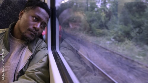A black man looking out of the window of a train to London, contemplating life