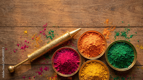 Top view flat lay of traditional brass pichkari (water gun) placed beside vibrant Holi powders in round metal bowls