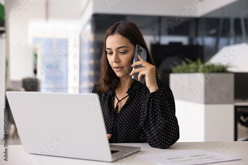 Slika na platnu Multitasking female professional talking on cellphone and typing on laptop at of