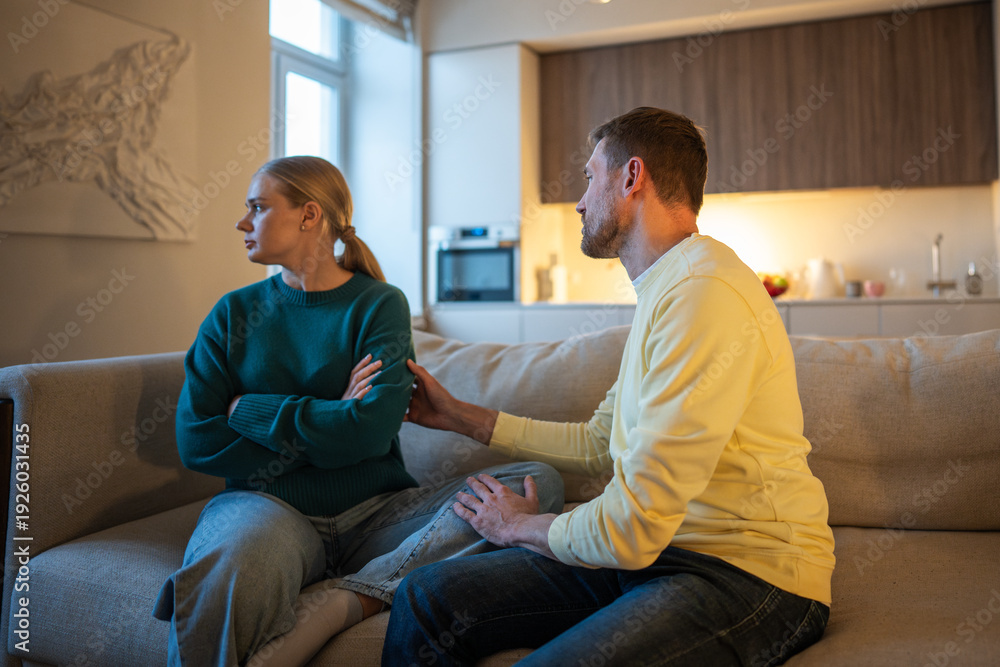 Obraz premium Narcissistic lying husband cheated on wife and attempting to ease couple conflict with stressed wife telling lies, stressed woman uninterested in male explanations sitting on sofa looking away.