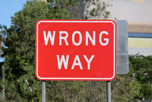 Red “Wrong Way” traffic sign beside a roadway with trees in the background