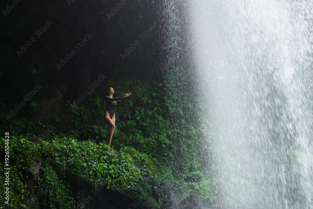 Fototapeta premium Playful Moment Under Waterfall Mist With Woman in Bodysuit, Bali Jungle