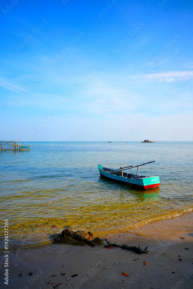 Fototapeta premium Landscape with traditional wooden boat in shallow water in Vietnam. Wooden oar-powered boat, painted blue and red, rests calmly in clear sea at shore. 