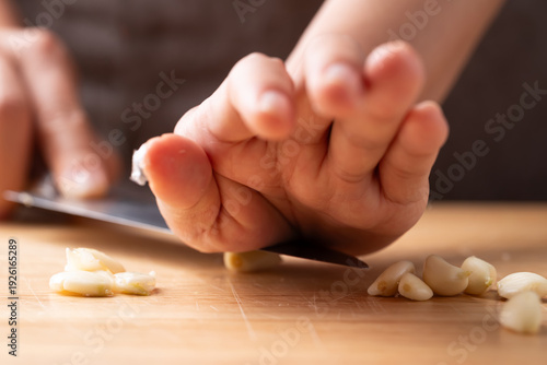 Foto Close up of hand crushing fresh garlic clove with a knife on a wooden cutting bo