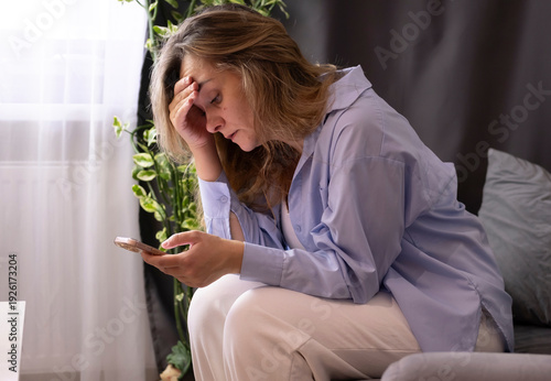 Foto sad middle-aged woman sitting on couch at home reading message on her phone
