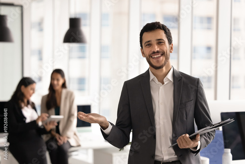 Foto Businessman holds clipboard stands confidently in coworking, looks at camera, ex