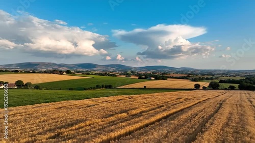 A vista showcases golden fields, rolling hills, and a dramatic sky with billowing clouds