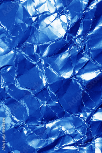 Close-up of a crumpled blue aluminum foil sheet showing metallic shine, creas...