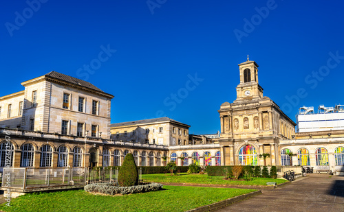 Scenic sunny view of the historic stone architecture, chapel clock tower, and green courtyard of the Lariboisiere Hospital in Paris, France.