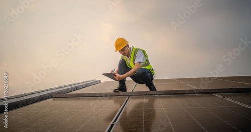 man in a yellow hard hat is writing on a clipboard while kneeling on a roof