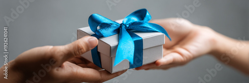 Two hands exchanging a small white gift box with a blue ribbon