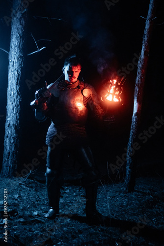 Bild auf Leinwand A knight in full armor, sword and torch in hand, walks through a gloomy night forest