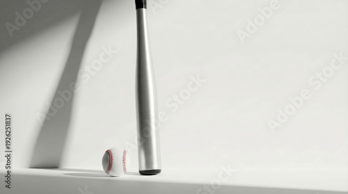 Minimalist studio photo of a metal baseball bat leaning near a baseball on white surface with dramatic shadows and copy space