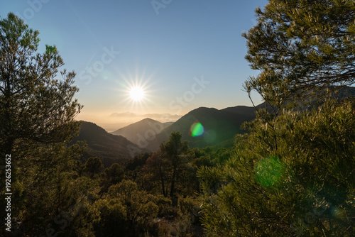 Mountain valley sunset creating sunburst with forest hills