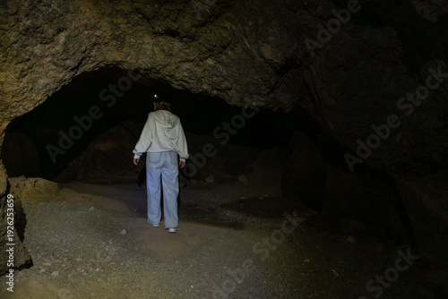 Person exploring dark underground cave with headlamp light
