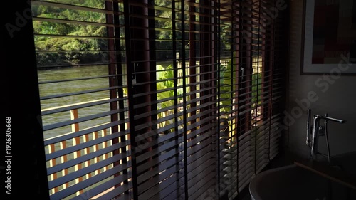 close-up image of blinds in the dark. The background is an abstract image. The blinds are brown against a background of flowing water. View from a bathroom in a resort.