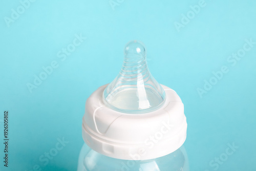 The top part of a baby bottle with a clear nipple. The background is a soft blue, focusing on the bottle. It is common for feeding infants.