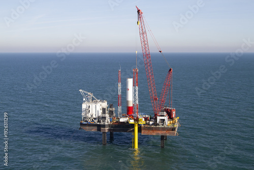 Netherlands, Netherlands - 13 February 2026: Aerial view of a vibrant red crane towering over an offshore platform, a stark contrast against the calm blue sea.
