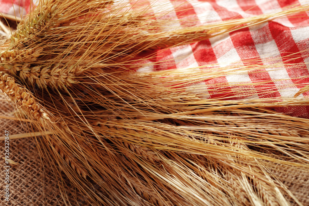 Fototapeta premium Wheat stalks and checked fabric on a burlap surface in a simple kitchen setting