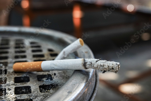 Cigarette butts in metal ashtray with smoke and ash. Burning cigarette butts in ashtray, Smoking concept close-up.