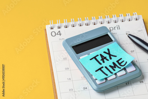 Tax time word on sticky note on calculator with calendar and pen on yellow background, accounting and financial planning, tax season concept