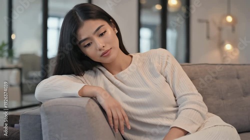 Pensive Young Woman Relaxing on a Sofa in a Modern Minimalist Living Room, 4K video