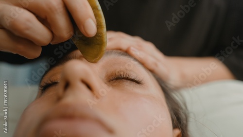 Relaxed woman enjoying jade facial massage in serene spa setting