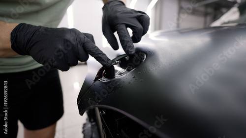 Close-up of a worker applying a matte black protective film on a car in a detailing shop.