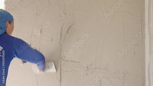 Female construction worker applying cement plaster with trowel on interior wall. Skilled labor, building renovation and equality in construction industry concept.