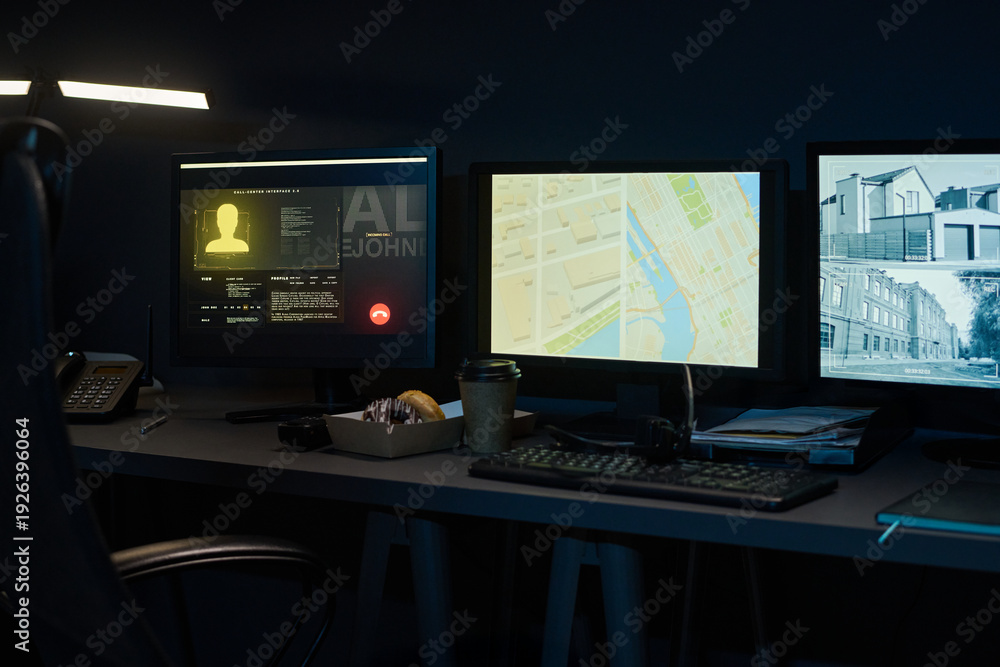 Naklejka premium Three computer monitors displaying digital map, surveillance footage, and user profile on dark desk with keyboard, telephone, takeaway coffee cup and pastry box in modern workspace