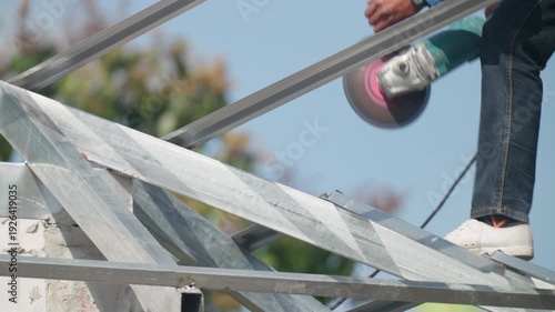 Construction technician drilling steel beam on roof structure against blue sky. Industrial metal framework, engineering precision and high level construction concept.