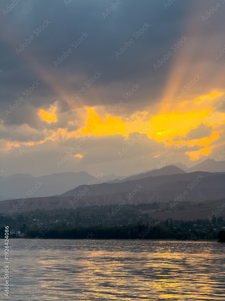 Fototapeta premium Sunset at Issyk Kul Lake in Kyrgyzstan. Bright sun breaking through clouds reflecting in clear turquoise water.