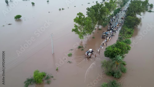 Aerial view of people crossing a completely flooded road in India, traveling in vehicles and on foot.

