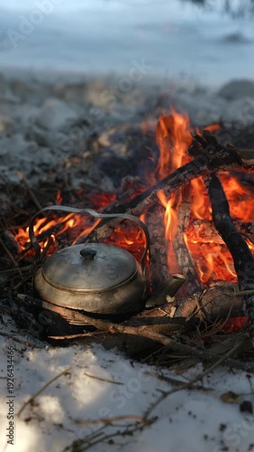 A camping kettle is boiling on the campfire coals. Hot tea on a winter hike. Winter camping. A bushcraft concept.