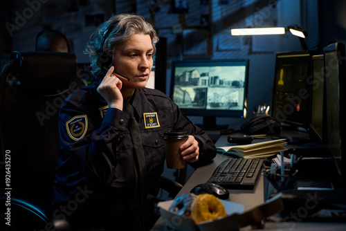 Tableau sur toile Middle aged Caucasian woman police officer sitting at desk wearing headset holdi