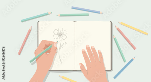 Overhead shot of hands using a green colored pencil to draw a flower in a sketchbook, surrounded by other pencils in pastel colors, conveying creativity.