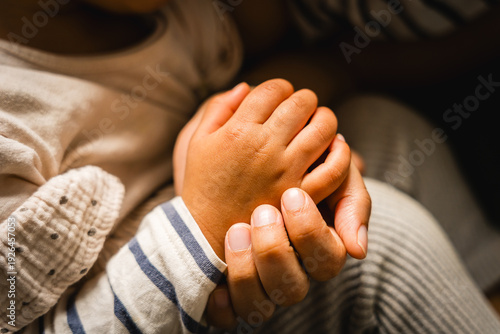Fotografie Close up of mother holding hands of hispanic baby toddler with sof light