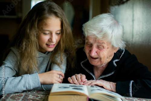 Grandmother and granddaughter reading a book together at home, sharing a warm intergenerational moment.