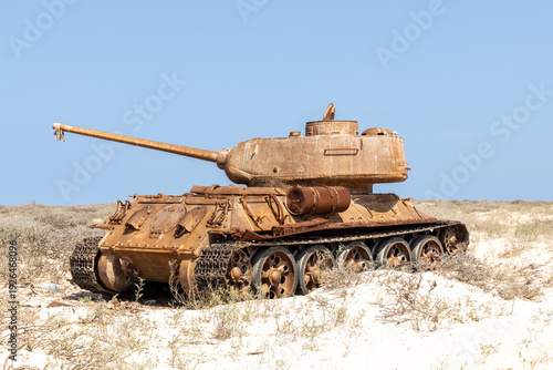 View of sun-bleached sand cradles a decaying tank, its rusted armor a stark contrast to the azure sky, whispering tales of forgotten conflicts, Qalansiyah, Socotra, Yemen.