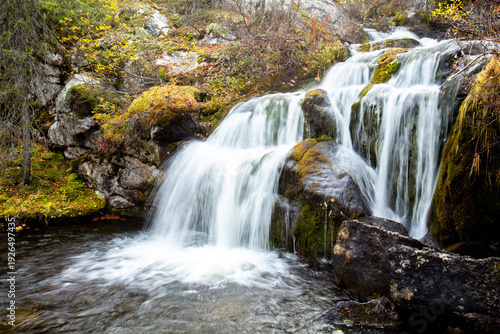 Long exposure of beautiful Kullaoja waterfall cascading on the rocks during autumn foliage near Naruska, Northern Finland, Europe