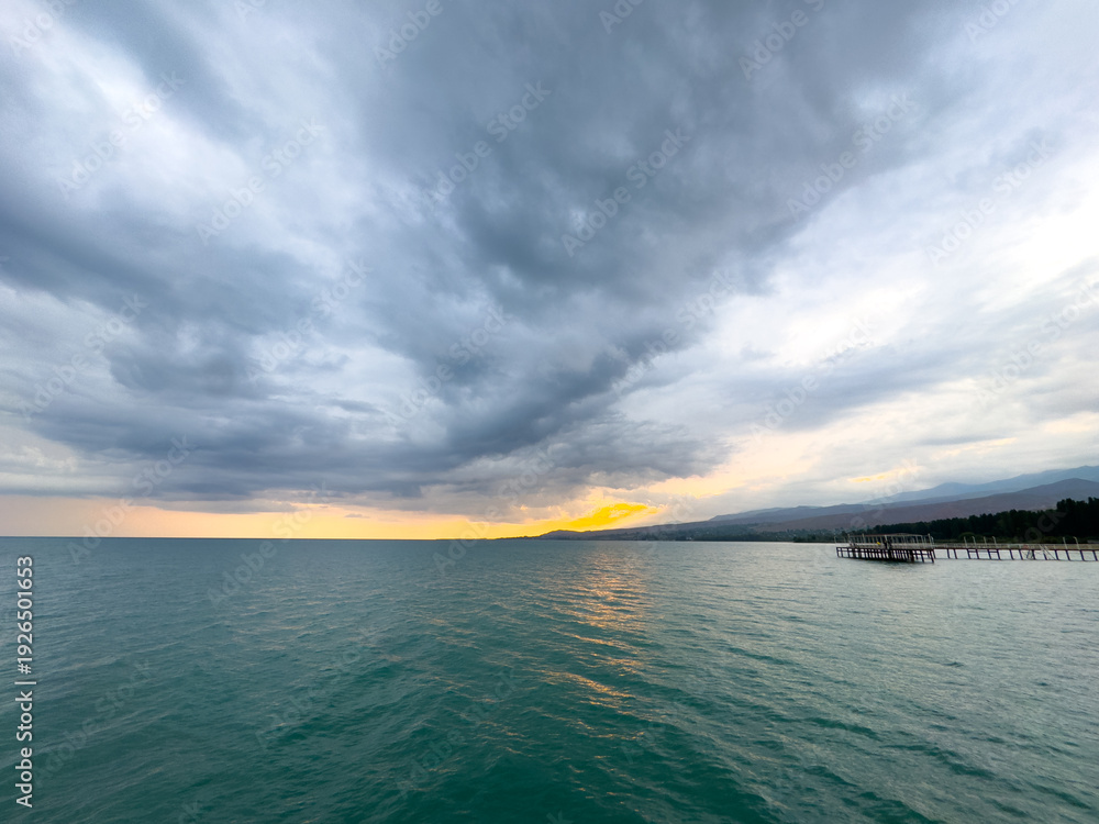 Obraz premium Sunset at Issyk Kul Lake in Kyrgyzstan. Bright sun breaking through clouds reflecting in clear turquoise water.