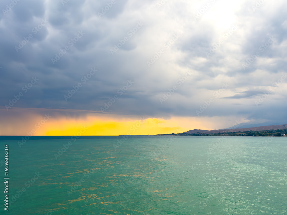 Fototapeta premium Sunset at Issyk Kul Lake in Kyrgyzstan. Bright sun breaking through clouds reflecting in clear turquoise water.