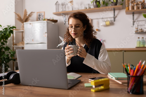 Vászonkép Curly young woman enjoys cozy moment in modern apartment while sipping tea
