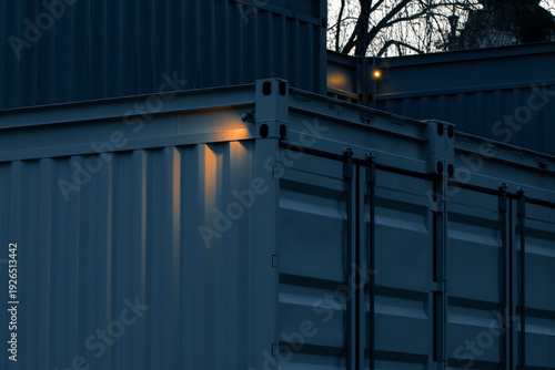 Stacked shipping containers at dusk with warm light reflecting on the corrugated metal surfaces